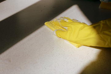 Hand in yellow rubber glove washing surface on a sunny day. Spring cleaning.brown color toned