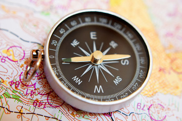 Round compass on colorful topographic map for orienteering or rogaining sport, close up view at shallow depth of field. Travel, recreation and active lifestyle concept.