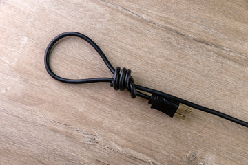 concept of energy dependence: hinge loop made of an electric cord with a plug, on a wooden background, selective focus