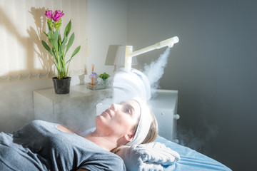 Beauty treatment of face with ozone facial steamer in beauty center. Beaultiful Blonde Girl.