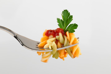 .Colored pasta on a fork with tomato sauce and a leaf of parsley close-up on a light gray background