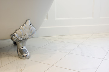Light gray claw foot tub on white marble floor and white wall wainscoting