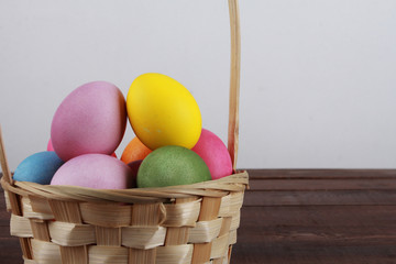 Painted eggs in basket on brown wooden table. Easter background concept. Pink, yellow, green, orange eggs, side view