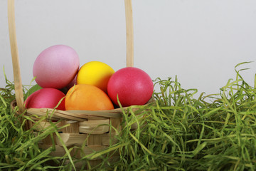 Painted eggs in basket with dry green grass. Easter background or egg hunt concept. Pink, yellow, green, orange eggs, hay, side view, close-up