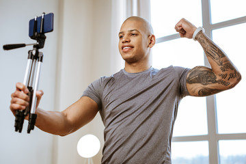 Dark-eyed bodybuilder using selfie stick while making photo