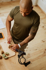 Sportsman with tattoo cutting kiwi while filming video about food