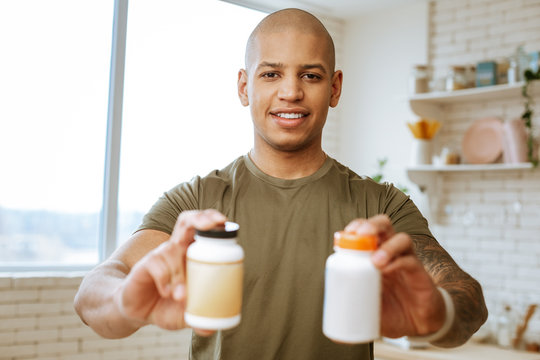 Dark-eyed man holding two packs of supplements for bodybuilders