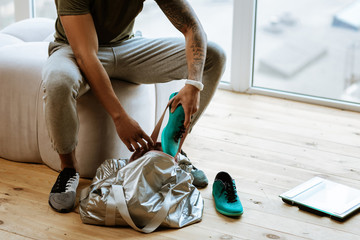 Dark-skinned sportsman with tattoo putting sneakers into bag