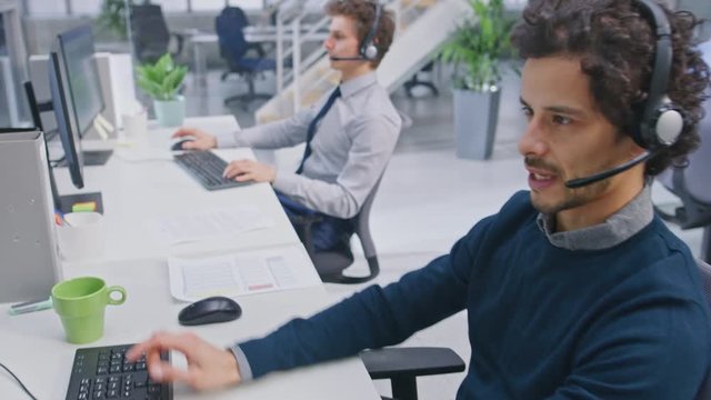 Team of Handsome and Beautiful Diverse Multicultural Customer Service Operators Working at a Busy Modern Call Center with Specialists Wearing Headsets and Actively Taking Calls. 