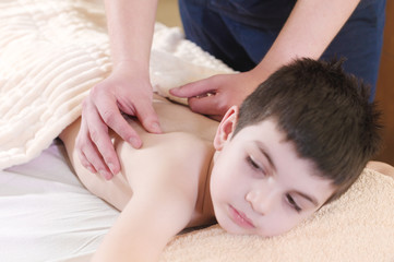 Fototapeta na wymiar A little boy relaxes from a therapeutic massage. Male massage therapist makes a medical massage to the back of a child