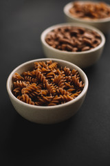 Variety of whole grain pasta, dark background, selective focus (fusilli pasta in focus), diagonal