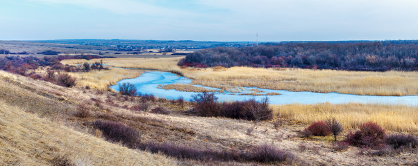 The panoramic view of the plain ice covered river with leafless forest and reed beds on the shore. Tuzlov river, Rostov-on-Don region, Russia