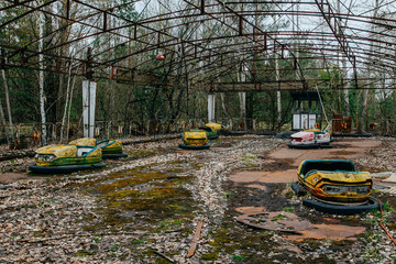 Old broken rusty metal radioactive yellow cars, children's electric cars, abandoned among...