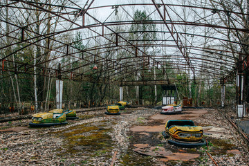 Old broken rusty metal radioactive yellow cars, children's electric cars, abandoned among...