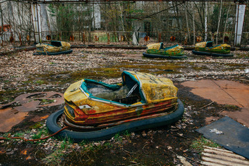 Old broken rusty metal radioactive yellow cars, children's electric cars, abandoned among...