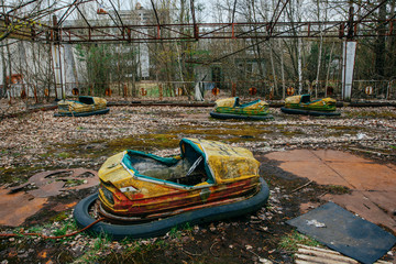 Old broken rusty metal radioactive yellow cars, children's electric cars, abandoned among...