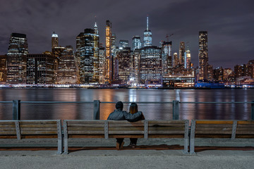 Scene of back side couple sitting and looking New york Cityscape beside the east river at the night...
