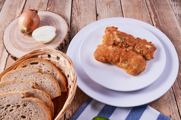 Deep-fried battered cod fillets, in a white plate next to onions and bread on a wooden background