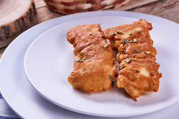 Deep-fried battered cod fillets, in a white plate next to onions and bread on a wooden background. Close-up