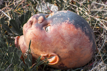 Creepy old doll head. Broken abandoned damaged scary toy in a garbage dump close-up. In the toy,...
