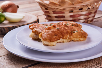 Deep-fried battered cod fillets, in a white plate next to onions, cucumber and bread on a wooden background. Close-up