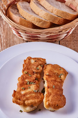 Deep-fried battered cod fillets, in a white plate next to bread on a wooden background. Close-up