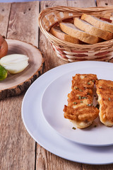 Deep-fried battered cod fillets, in a white plate next to onions, cucumber and bread on a wooden background. Close-up