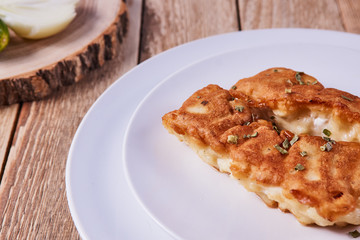 Deep-fried battered cod fillets, in a white plate next to onions on a wooden background. Close-up