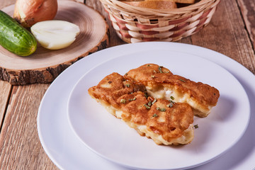 Deep-fried battered cod fillets, in a white plate next to onions, cucumber and bread on a wooden background. Close-up