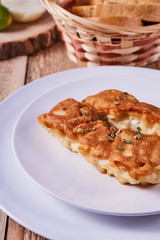 Deep-fried battered cod fillets, in a white plate next to onions, cucumber and bread on a wooden background. Close-up