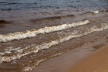 Waves with foam on a sunny summer day. Sandy beach
