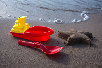 Fototapeta na wymiar Ship and scoop - children's toys and starfish made of sand. Sandy beach, sunny day.