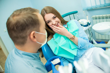 Beautiful emotional girl sitting in a dental chair next to a male doctor. Dental clinic. Doctor and...