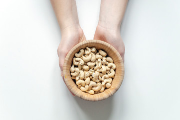 Women's hands holding a wooden plate with cashew nuts. The concept of proper nutrition and healthy lifestyle. The free space of the white background.