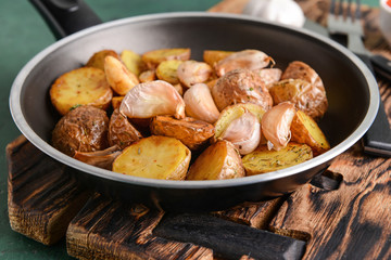 Frying pan with tasty baked potato on wooden board
