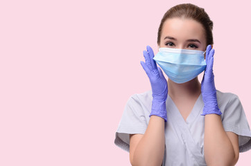 Beautiful female doctor or nurse wearing protective mask and latex or rubber gloves on light pink background isolated with copyspace. Health care concept