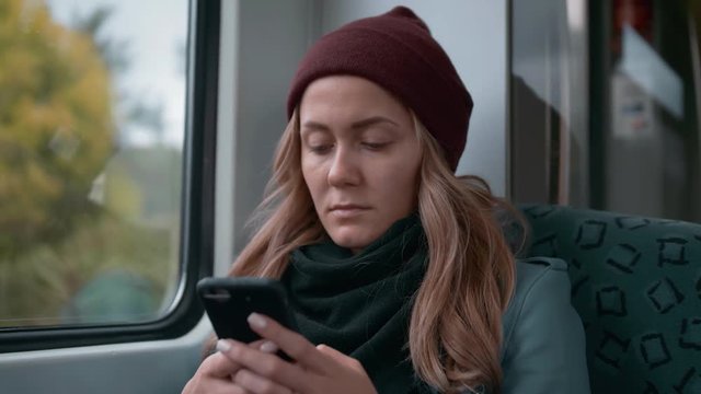 young Caucasian girl in a red cap rides on a subway or tram train car, uses the phone, prints a message. Slow Motion.
