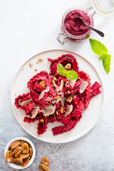 Top view of vegetarian mafaldine pasta with beet pesto sauce, walnut and parmesan cheese on a white background