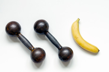 Two metal brutal dumbbells on a white background, top view close-up. Next is a banana, the concept of proper nutrition and a healthy lifestyle.