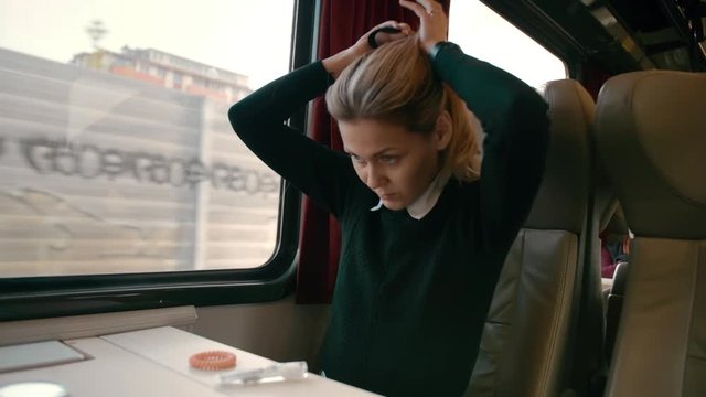 Young caucasian girl rides in a luxury intercity train carriage. Makes a hairstyle out of hair. Concept of how to be beautiful while traveling. slow motion.