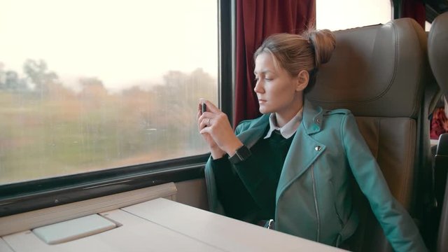 Young caucasian business woman is traveling in a luxury intercity train carriage. Uses a mobile phone for photos. Slow Motion.