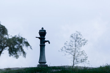Old, vintage water pump on a small hill with two trees in the background 