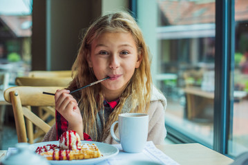 Happy nice little girl at cafe.The child sits at a table in a cafe and is happy.A happy childhood,...