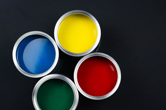 Four Open Cans Of Paint On A Black Background.