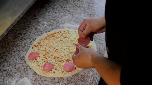 Pizza baking preparation. Chef applies pepperoni slices on the pizza before baking.