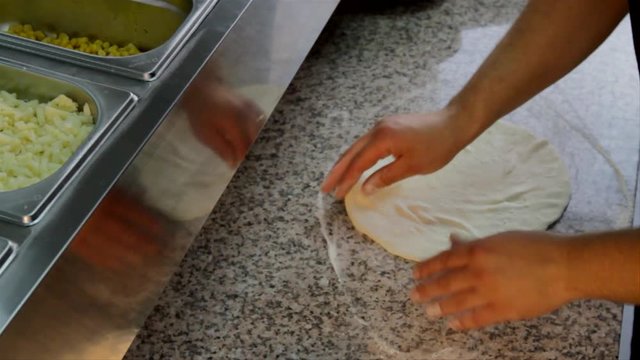 Pizza baking preparation. Chef picks up a piece of dough, flours it and starts to spread it with his hands.