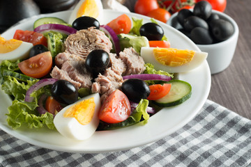 Fresh Caesar tuna salad with delicious tuna fish, ruccola, spinach, cabbage, arugula, egg, parmesan and cherry tomato on wooden background. Oil, salt and pepper. Healthy and diet food concept.