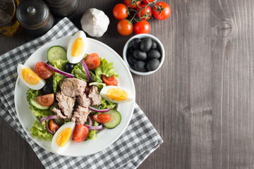 Fresh Caesar tuna salad with delicious tuna fish, ruccola, spinach, cabbage, arugula, egg, parmesan and cherry tomato on wooden background. Oil, salt and pepper. Healthy and diet food concept.