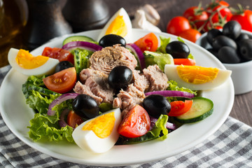 Fresh Caesar tuna salad with delicious tuna fish, ruccola, spinach, cabbage, arugula, egg, parmesan and cherry tomato on wooden background. Oil, salt and pepper. Healthy and diet food concept.