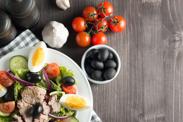 Fresh Caesar tuna salad with delicious tuna fish, ruccola, spinach, cabbage, arugula, egg, parmesan and cherry tomato on wooden background. Oil, salt and pepper. Healthy and diet food concept.